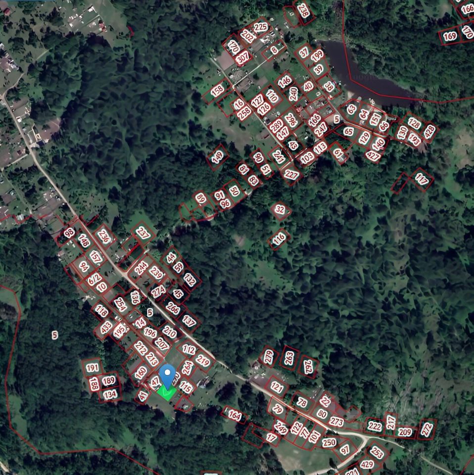 На изображении представлены участки земли, обозначенные номерами, расположенные среди зеленых насаждений. Участки имеют четкие границы, обозначенные красным цветом. Некоторые участки имеют прямоугольную форму, другие - более произвольную. В центре видна небольшая группа участков, которые образуют более плотную застройку. Дорога проходит вдоль одного из краев, связывая участки. Лесные массивы окружают территорию, создавая ощущение уединенности и близости к природе. Визуально пространство выглядит организованным и планируемым, что может быть интересно для застройщиков или покупателей.